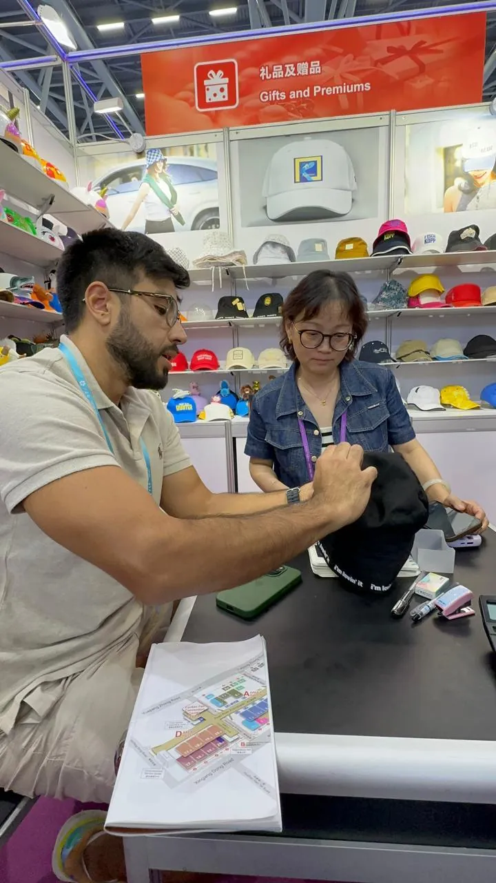 João conferindo um boné com uma fornecedora no estande de brindes de uma feira na China